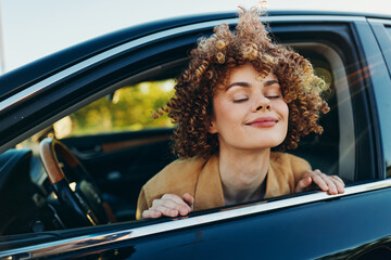 Fototapeta premium A woman with curly hair leans out of a car window, eyes closed, smiling gently as the breeze touches her face. A candid lifestyle moment with retro film color tones, conveying relaxed mood, freedom,