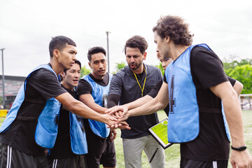 Obraz premium Soccer team and coach stacking hands to unify and motivate before a match. Teamwork, shared goal, and professional leadership concept in sports.