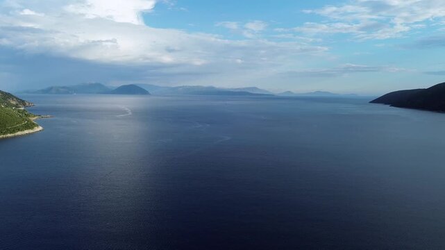 Wide aerial drone shot over the deep blue waters of Vasiliki bay in Lefkada island, looking towards Ithaca and Kefalonia islands under a cloudy sky. High quality 4K travel footage.