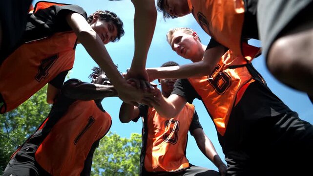 Soccer players stacking hands together in a team huddle before a match, demonstrating unity, teamwork, and determination on the football field