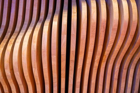 A full-frame shot of a decorative architectural wall feature consisting of numerous vertical, closely arranged wooden slats with unique curved profiles, creating a rhythmic wave-like pattern.