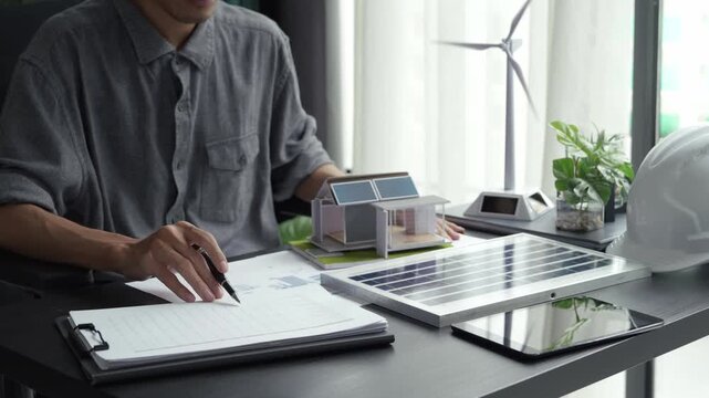 Electrical engineer working on blueprint with solar panel model sustainable energy concept