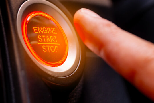 The driver's hand is pressing the car start button. Concept of transportation and technology	
