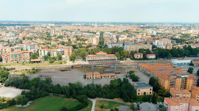 Modena, Italy. Piazza Manzoni railway station, eclectic 1932 passenger building with Corinthian pilasters and curved pediment, Drone footage over the city under bright summer sky. Drone footage, Depa