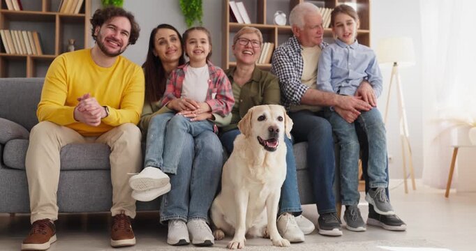 Family grandparents parents children with labrador dog. Smiling together at home on a cozy sofa, indoor portrait with friendly pet and relaxed weekend mood. Theme of happy family unity.