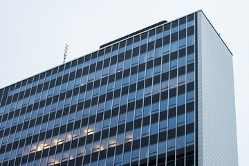 Obraz premium Modern office building with reflective glass windows and metal facade, showcasing multiple floors and antennas on the rooftop against a clear sky