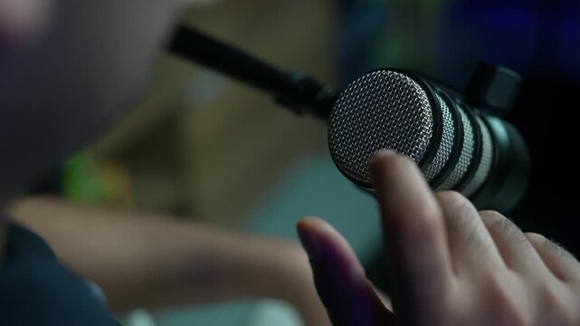 slow motion of presenter finger touching the metallic mesh grille of a professional microphone in a podcast studio. Sound testing, audio engineering and broadcast setup concept.