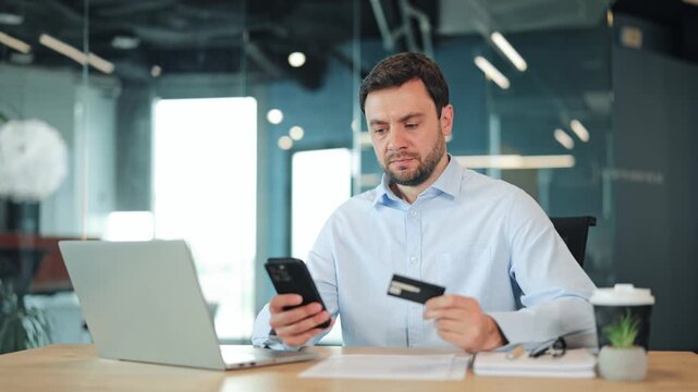 Frustrated businessman or IT specialist experiencing declined credit card transaction on smartphone. Annoyed corporate worker, manager or freelance designer having failed online payment at desk.