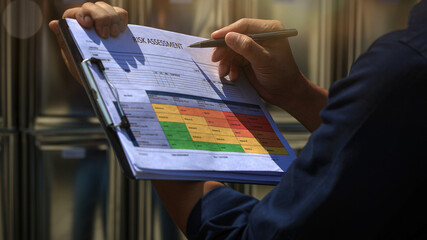 Focused worker conducts serious maintenance risk review holding clipboard with safety chart and pen during careful industrial inspection © Piya W.
