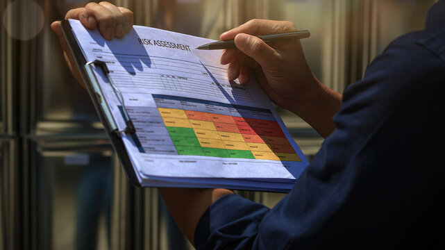 Focused worker conducts serious maintenance risk review holding clipboard with safety chart and pen during careful industrial inspection