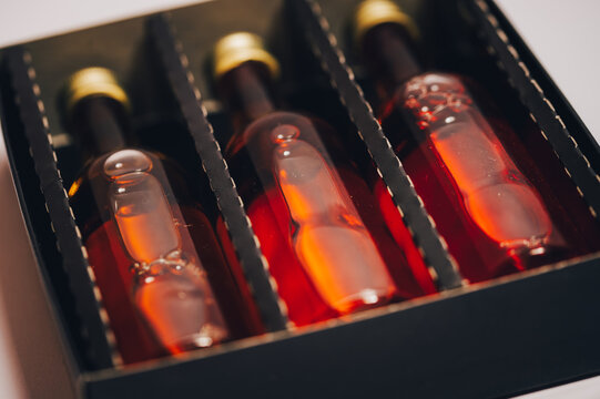 Three miniature amber glass bottles with golden caps in a luxury black gift box.Premium collection set of alcohol or gourmet syrup bottles in a partitioned package.High-angle close-up of a sophisticat