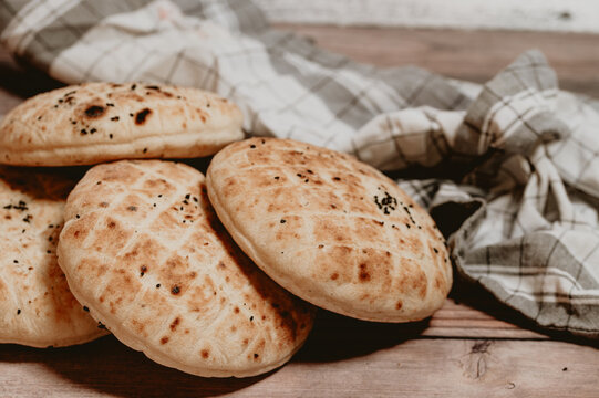 Stack of freshly baked pita bread flatbreads on a wooden table.Traditional homemade flatbread loaves with black cumin seeds on wood.Close-up of golden brown grilled pita breads with rustic kitchen clo