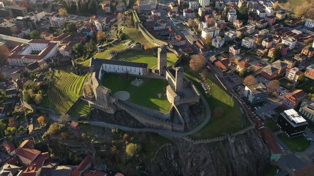 Aerial view of Castel Grande with its ancient stone walls and green courtyards overlooking the urban landscape during sunset in Bellinzona, Ticino, Switzerland.