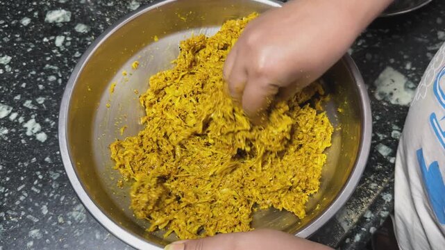Static close shot of hands mixing shredded raw mango with spices and mustard oil inside a steel bowl during homemade Indian pickle preparation on a kitchen countertop