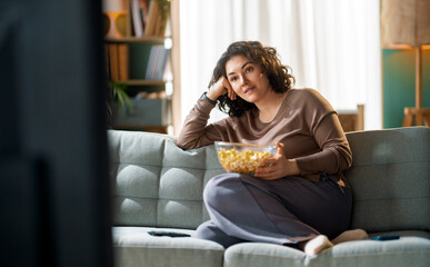 Obraz premium Relaxed Woman Watching TV at Home with Popcorn on Cozy Sofa in Living Room