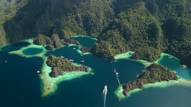 Aerial high altitude parallax shot above Twin Lagoon showing limestone karst islands with turquoise lagoons and boats in Coron Palawan Philippines