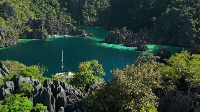 Aerial flypass beside luxury catamaran yacht with solar panels surrounded by dramatic limestone karst mountains and turquoise water at Twin Lagoon in Coron Palawan Philippines