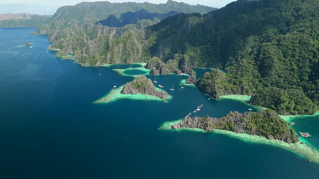High altitude aerial flyover above karst limestone islands and turquoise lagoons of Twin Lagoon archipelago in tropical paradise of Coron Palawan Philippines