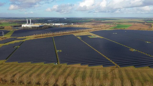 Drone shot framing rows of blue solar photovoltaic panels next to a natural gas power plant