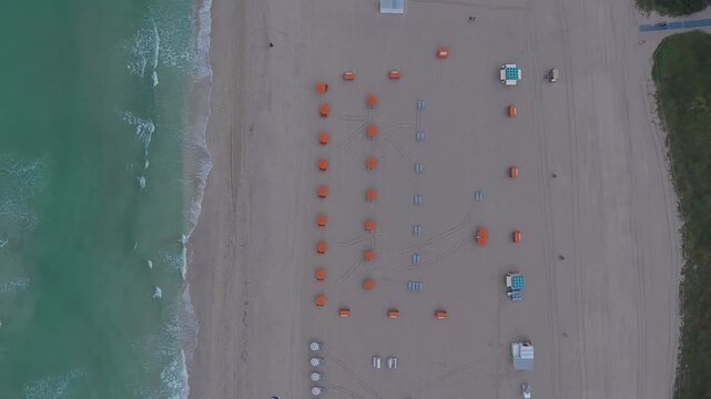 Aerial view of South Beach featuring rows of orange umbrellas on the sand and turquoise ocean waves in Miami Beach, Florida, United States.