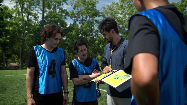 Soccer coach explaining tactics and game strategy to players during a team briefing on an outdoor football field before a match