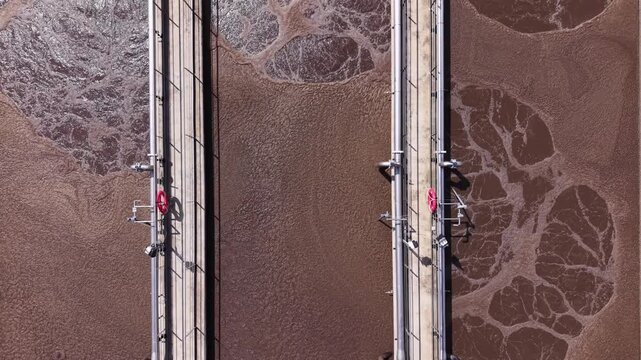 Top-down aerial view of aeration basins with activated sludge swirling in circular patterns at a modern wastewater treatment facility, showing biological treatment process