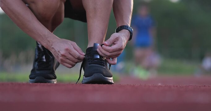 Cinematic low angle close-up of a male runner crouching and tying shoelaces of a black running shoe on an outdoor track