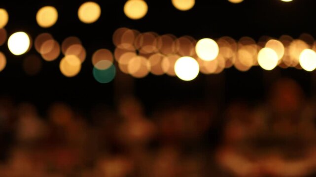 Blurred bokeh video of warm golden party lights hanging at an outdoor night event, representing celebration, festivals, wedding receptions, luxury gatherings, and a cozy festive atmosphere.