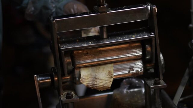 Close-up of a street food vendor using a traditional metal roller machine to crush and flatten dried squid, illustrating authentic Asian street food preparation and local culinary culture