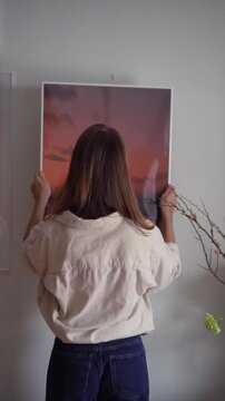 Woman hanging large framed sunset picture on wall