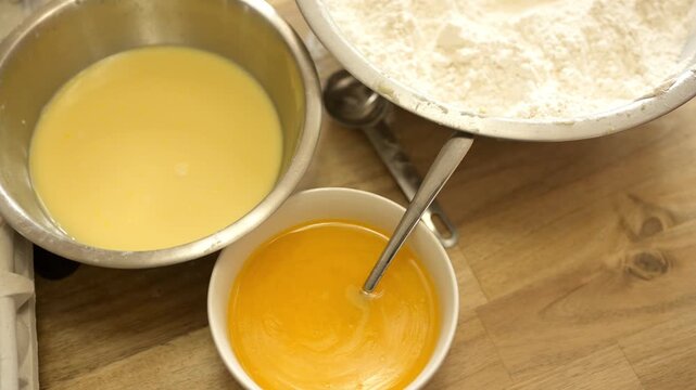 Overhead view of egg mixtures and flour bowls on wooden table