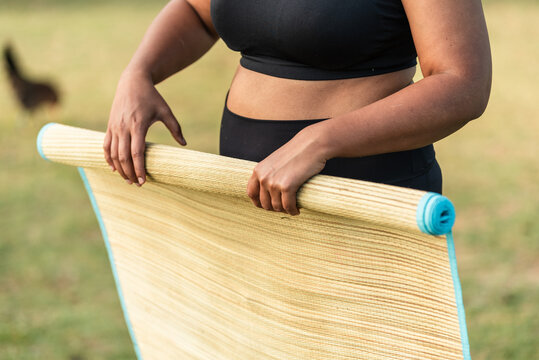 Woman rolling a straw yoga mat outdoors after the yoga session