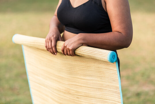 Woman rolling a straw yoga mat outdoors after the yoga session