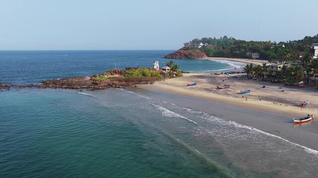 Aerial view of the turquoise waters and sandy shores of Kovalam Beach with fishing boats and rocky outcrops under a clear sky in Kovalam, Kerala, India.