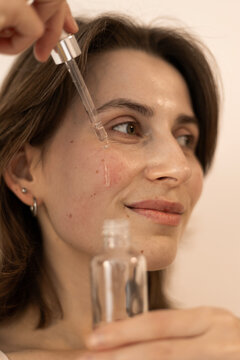Young woman applying beauty serum with dropper on her cheek for