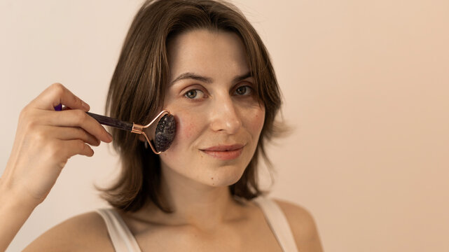 Young woman applies textured stone facial roller to cheek for sk