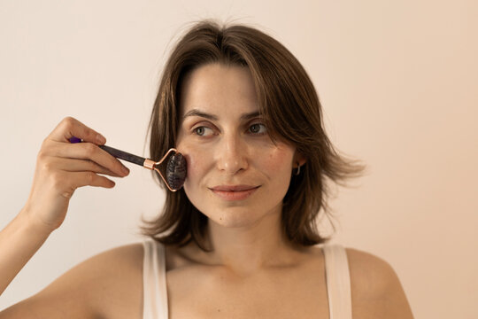 Young woman applying textured stone facial roller for healthy sk