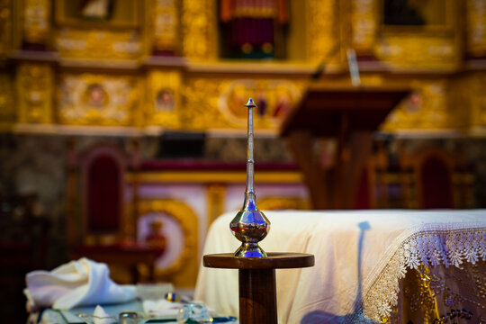 A silver holy water sprinkler, also known as an aspergillum, resting on a small wooden stand inside a church for blessing and baptism rituals.