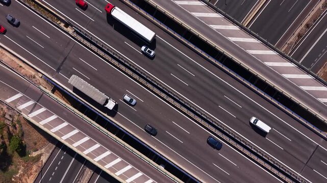 Top-down overhead view of a multi-lane highway interchange with cars and trucks in motion, featuring road markings, barriers, and surrounding vegetation