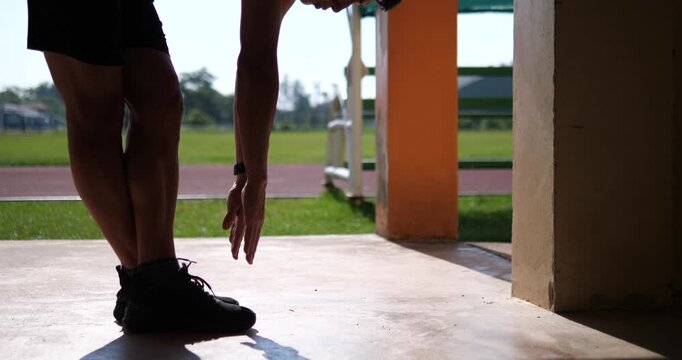Cinematic low angle shot of a male athlete doing a standing forward fold to stretch hamstrings and touch toes on track, sports conditioning concept