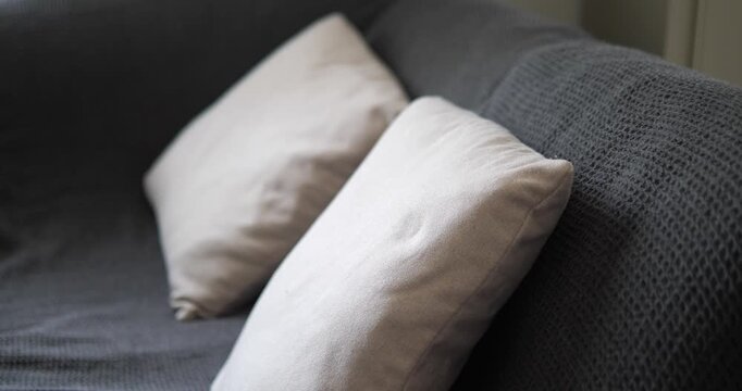 Cinematic close-up of soft cream pillows on a dark grey sofa couch with a textured knitted blanket, cozy home interior design concept