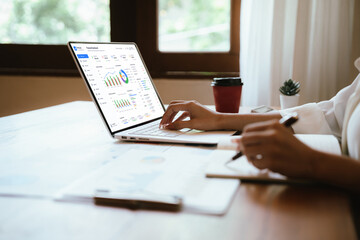 Fototapeta premium Professional working on a laptop at a home office desk with documents and reports, representing remote work, digital business, productivity, data analysis, and modern workplace efficiency.