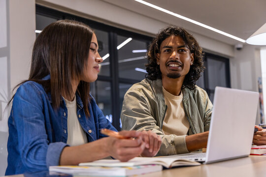 Asian woman and Indian man writing with pencil by notebooks and laptop at modern study table