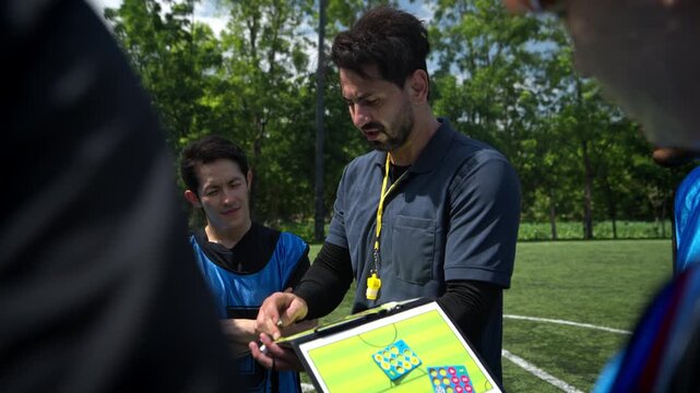 Soccer coach explaining tactics and game strategy to players during a team briefing on an outdoor football field before a match