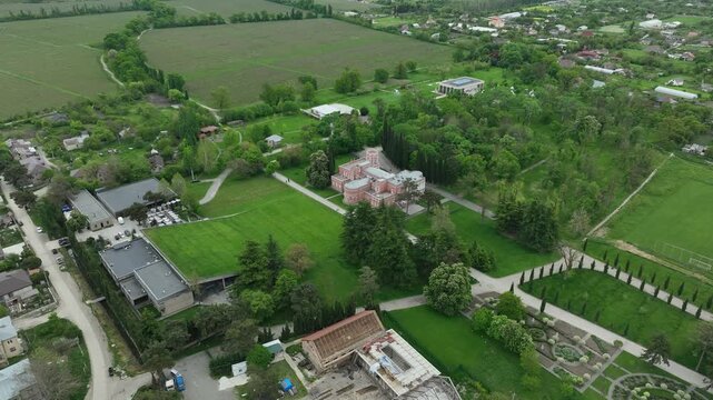 Aerial view of Chateau Mukhrani royal palace and estate in Georgia, magnificent pink castle architecture with a tower surrounded by a lush green park, gardens and pathways on a spring day.