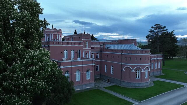 Aerial view of Chateau Mukhrani royal palace and estate in Georgia, magnificent pink castle architecture with a tower surrounded by a lush green park, gardens and pathways on a spring day.