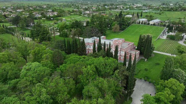 Aerial view of Chateau Mukhrani royal palace and estate in Georgia, magnificent pink castle architecture with a tower surrounded by a lush green park, gardens and pathways on a spring day.