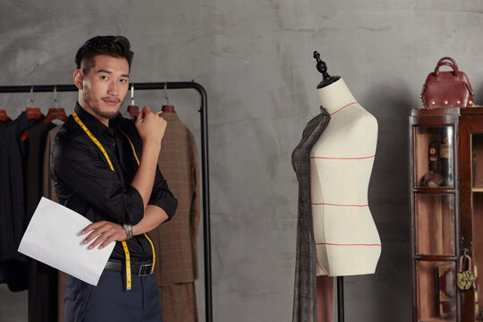 Confident fashion designer in tailoring studio with dress form
