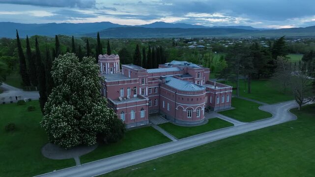 Aerial view of Chateau Mukhrani royal palace and estate in Georgia, magnificent pink castle architecture with a tower surrounded by a lush green park, gardens and pathways on a spring day.