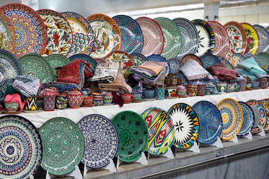 Colorful hand-painted Uzbek ceramic plates and cups displayed at Siab bazaar in Samarkand. Traditional pottery and textiles make a vibrant market stall, ideal for travel and cultural content.